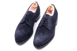 Eleganckie z ażurkami i dekoracyjnymi zdobieniami obuwie zamszowe koloru granatowego typu brogues ze gumową podeszwą. Szyte metodą ramową.