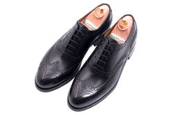 Eleganckie skórzane obuwie z ażurkami i dekoracyjnymi zdobieniami koloru czarnego typu brogues z gumową podeszwą. Szyte metodą ramową.